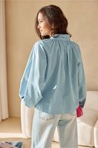Woman wearing a light blue pleated blouse in a room with beige walls and a white couch.