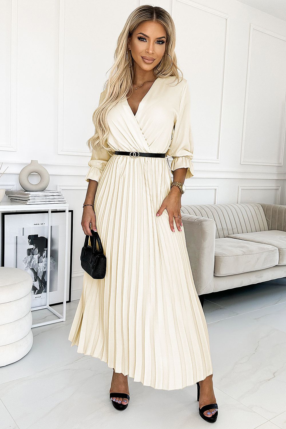 Woman in a white pleated dress standing in a modern living room.
