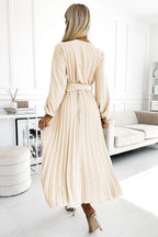 Woman in a beige pleated dress standing in a modern living room.