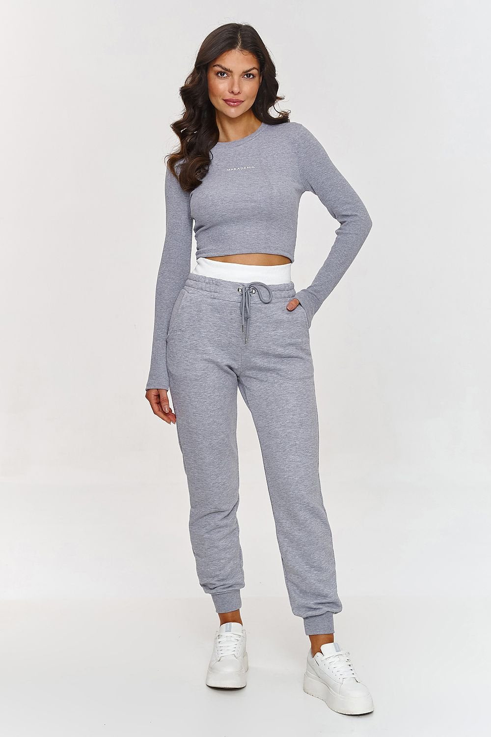 Woman wearing a gray long-sleeve top and jogger pants on a white background