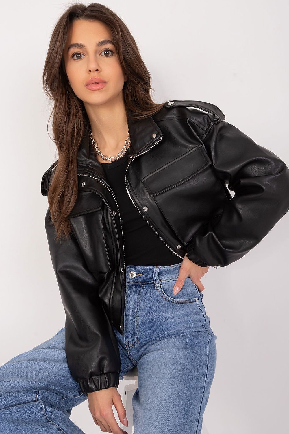 Woman wearing a black leather jacket and blue jeans against a white background