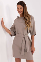 Woman wearing a beige dress with a belt against a white background