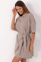 Woman wearing a beige dress with a belt on a white background