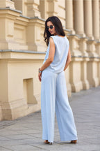 Woman wearing a light blue jumpsuit standing in front of a beige building.