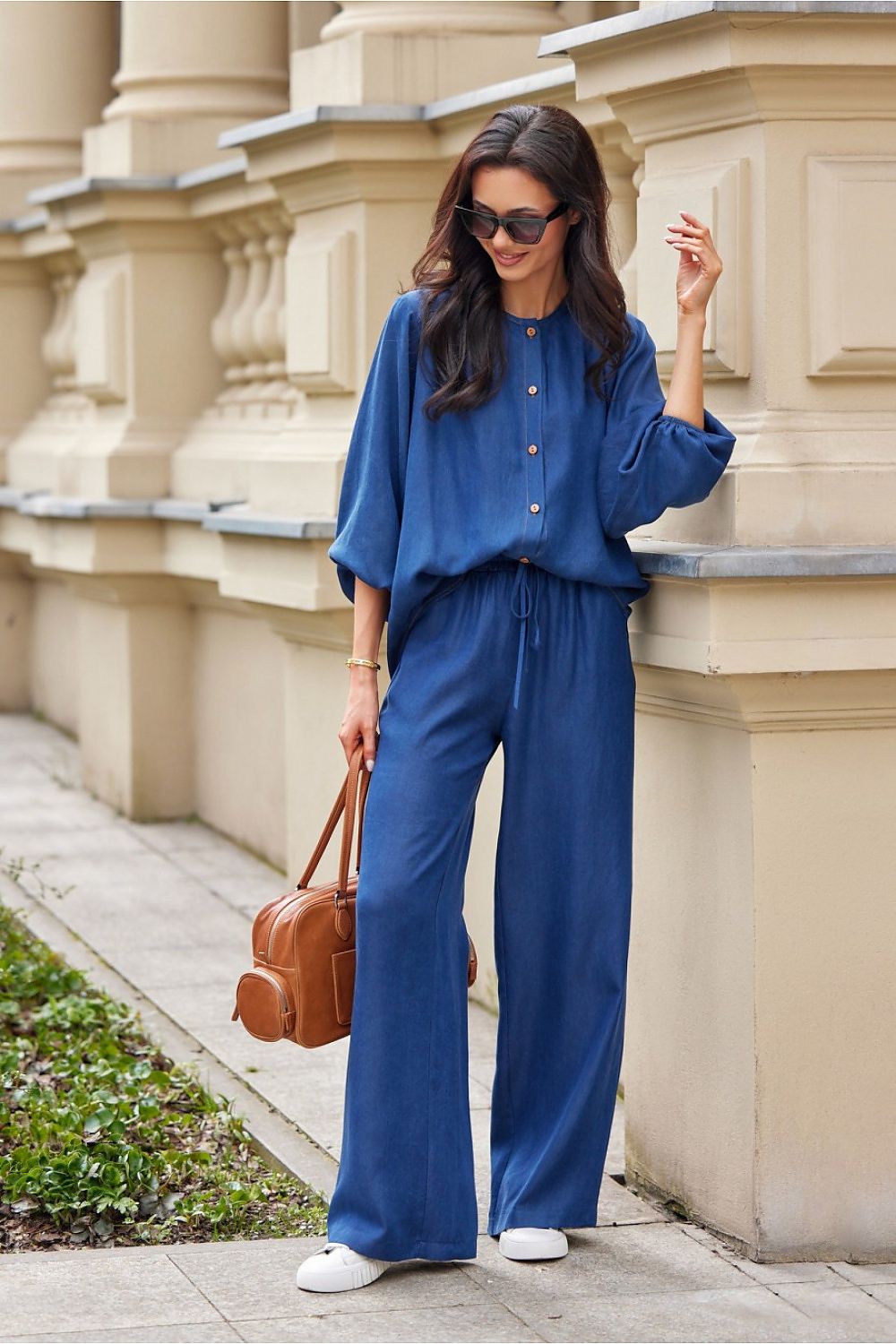 Woman in a blue outfit standing against a beige architectural wall.