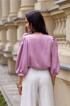 Woman wearing a pink blouse and white pants standing in front of architectural columns.