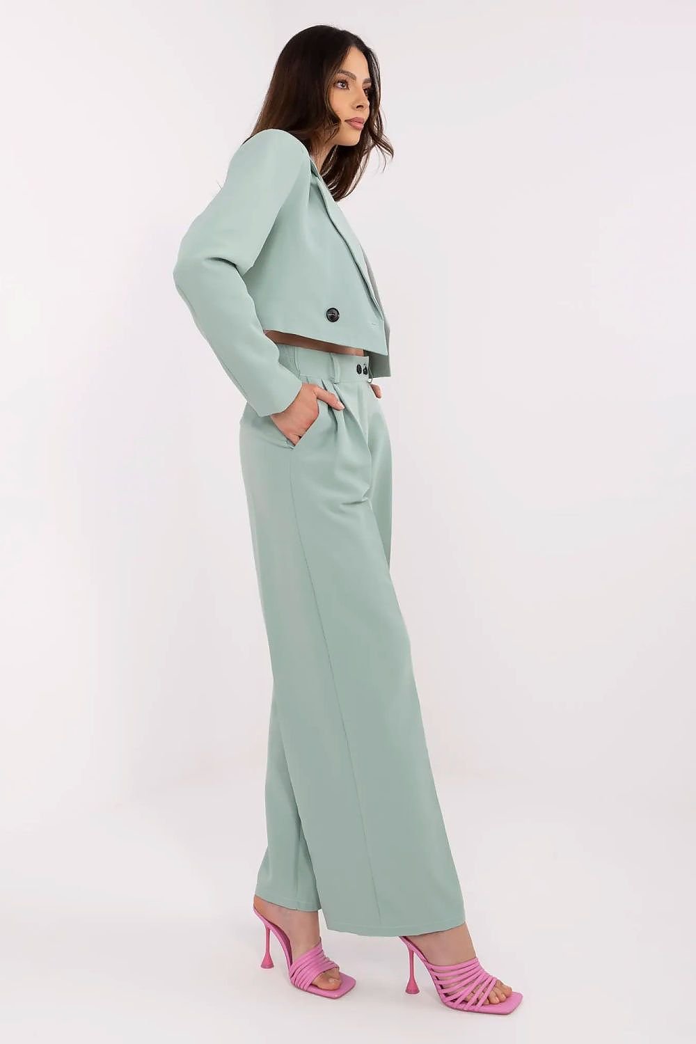 Woman wearing a light green suit with pink shoes on a white background