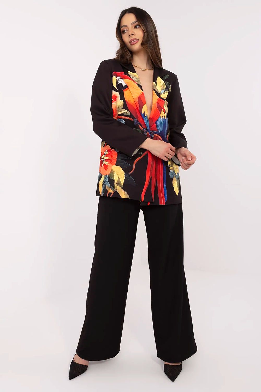 Woman wearing a colorful parrot-patterned blazer over a black outfit on a white background