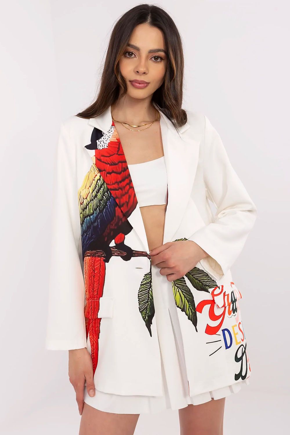 Woman wearing a white blazer with a colorful parrot design on a plain background