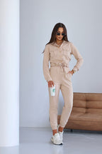 Woman in beige jumpsuit holding a Starbucks cup against a plain background