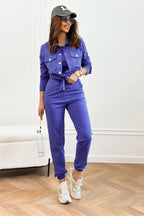 Woman in a blue jumpsuit with a cap and sunglasses, standing indoors.