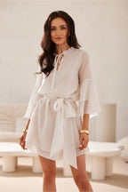 Woman wearing a white dress with long sleeves in a minimalistic room.