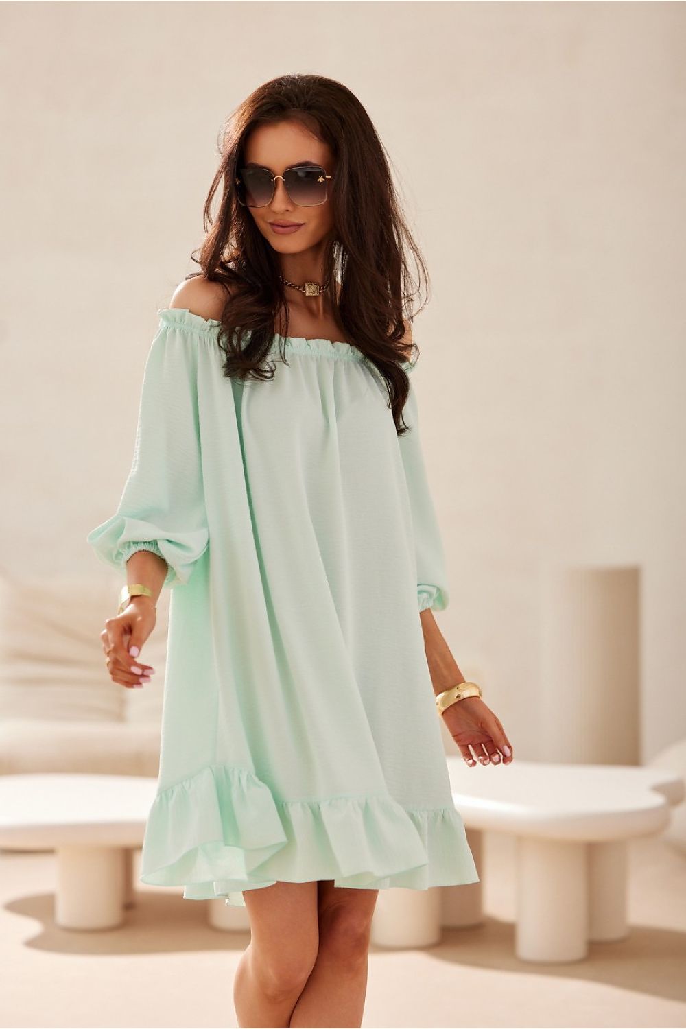 Woman wearing a light green off-shoulder dress in an indoor setting.