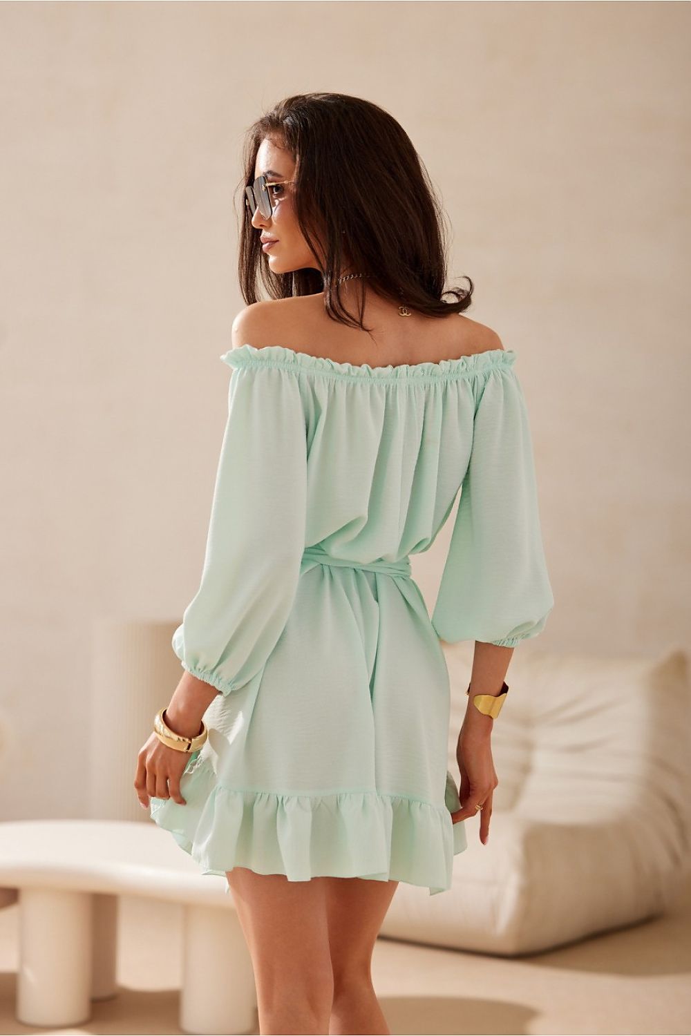 Woman wearing a light green off-shoulder dress in a minimal indoor setting