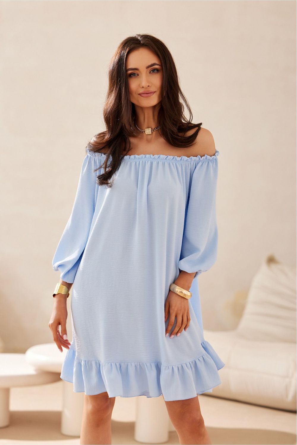 Woman wearing a light blue off-shoulder dress in a neutral setting