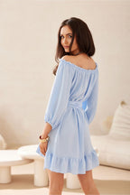 Woman wearing a light blue off-shoulder dress in a neutral setting