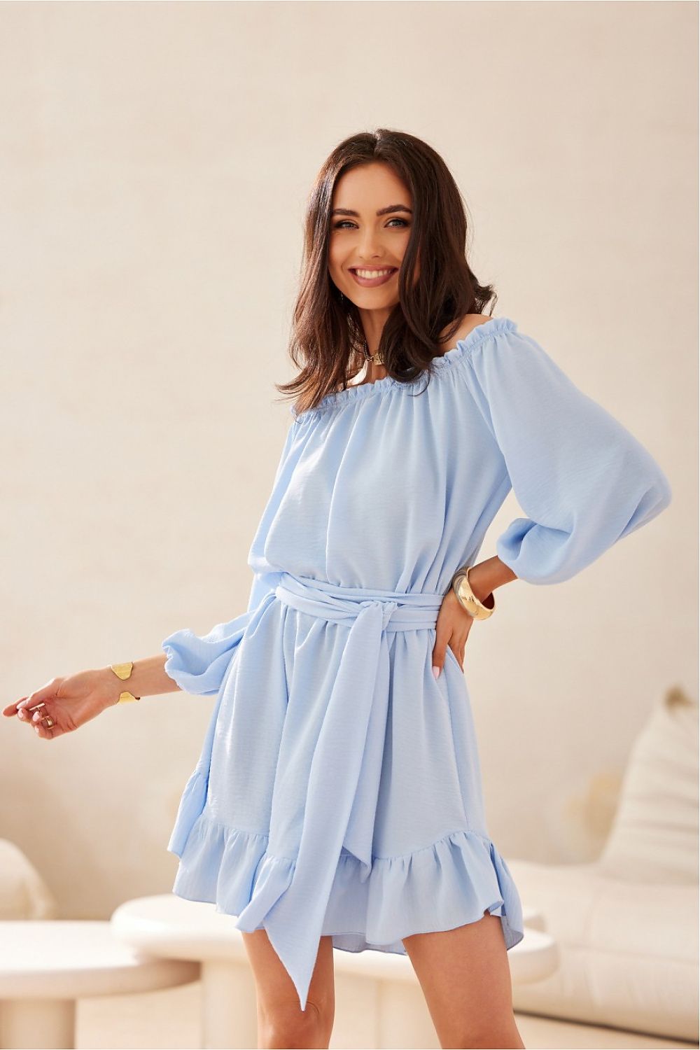 Woman wearing a light blue dress with ruffled sleeves and hem in a neutral setting.