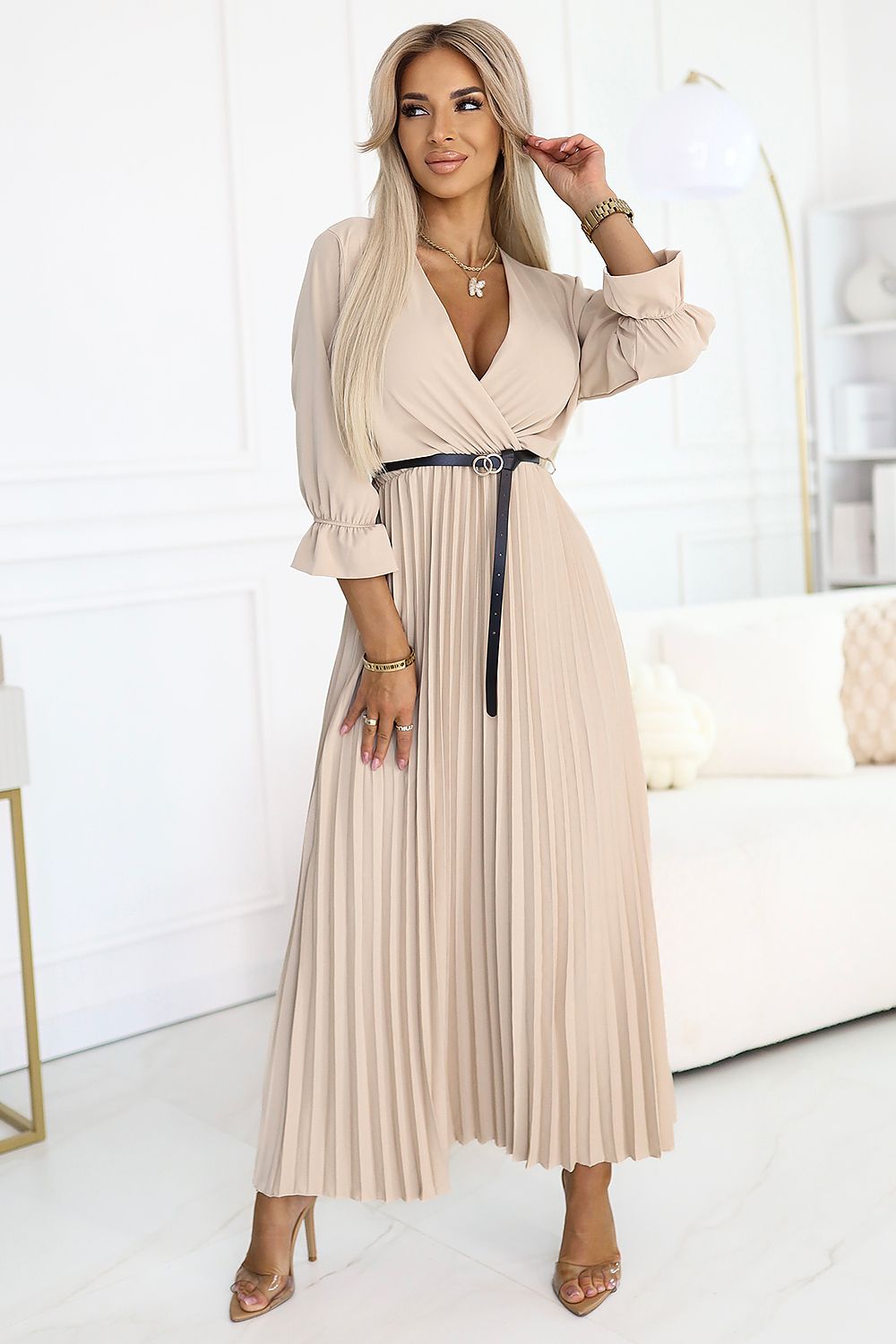 Woman wearing a beige pleated dress in a bright room.