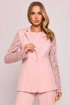 Woman wearing a pink suit with lace sleeves against a plain background