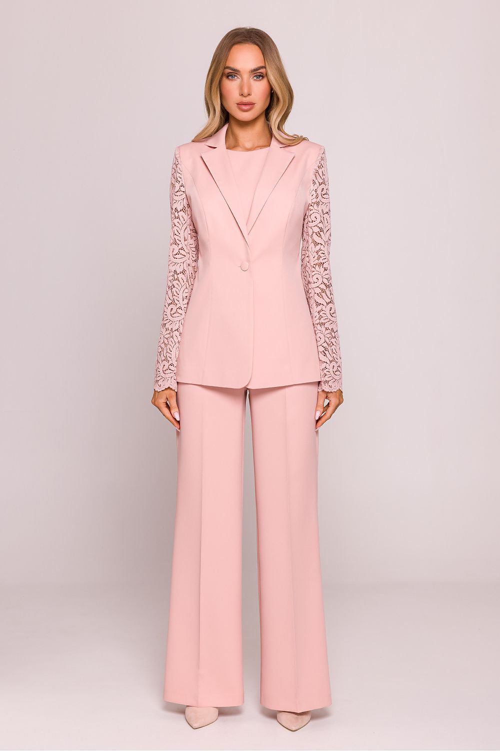 Woman wearing a pink suit with lace sleeves on a light pink background