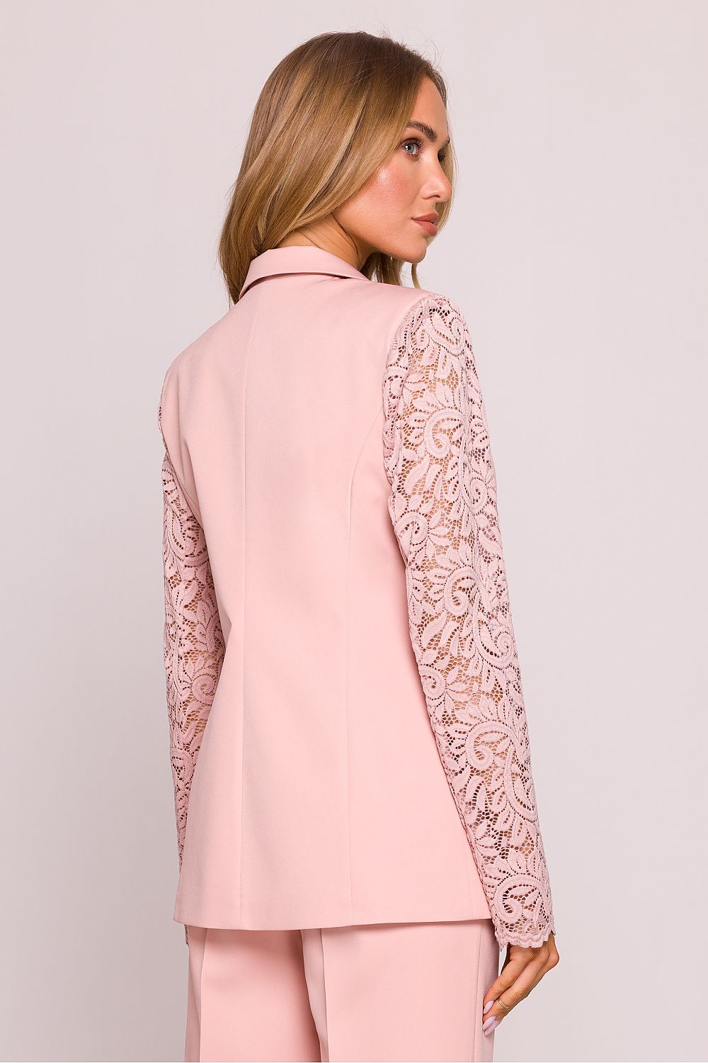 Woman wearing a pink outfit with lace sleeves on a light background