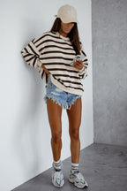 Person wearing a striped sweater, denim shorts, and white sneakers against a plain wall.