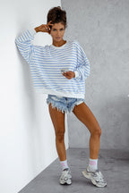 Woman wearing a blue and white striped sweater and denim shorts against a gray wall.