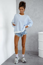 Woman wearing a blue and white striped sweater with denim shorts against a gray wall.