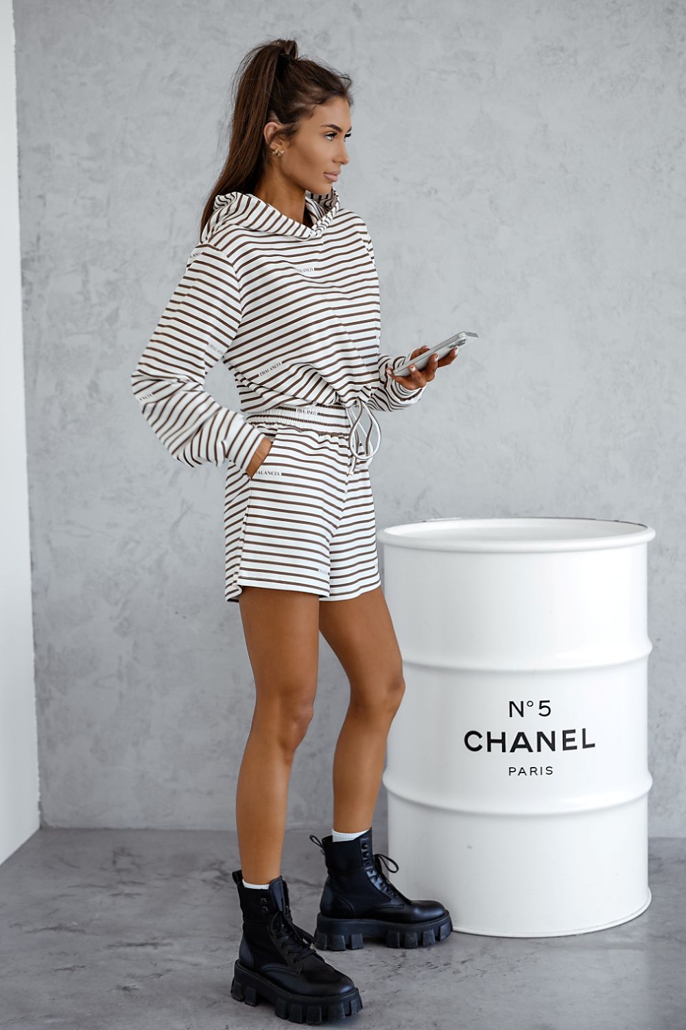 Woman in striped outfit standing next to a Chanel barrel.