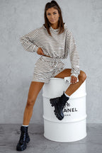 Woman in striped outfit sitting on a Chanel barrel-shaped stool against a gray background