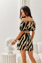 Woman wearing a zebra print off-shoulder top and skirt in a white room.