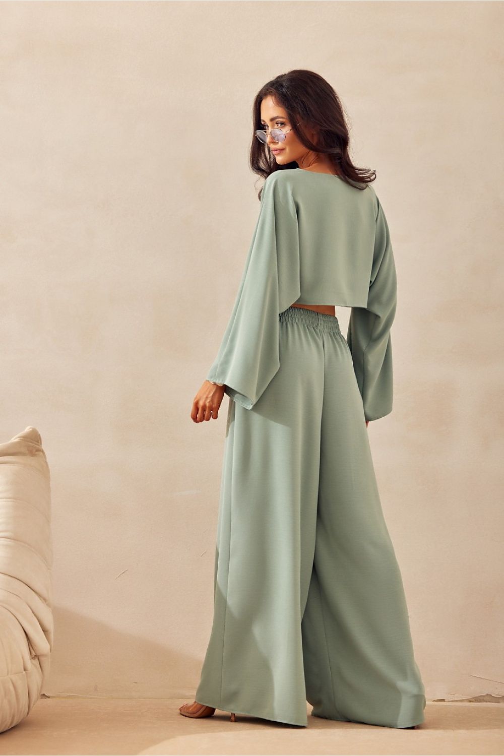 Woman wearing a green outfit standing against a beige background