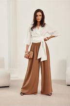 Woman wearing a white blouse and brown wide-leg pants in a minimalistic setting