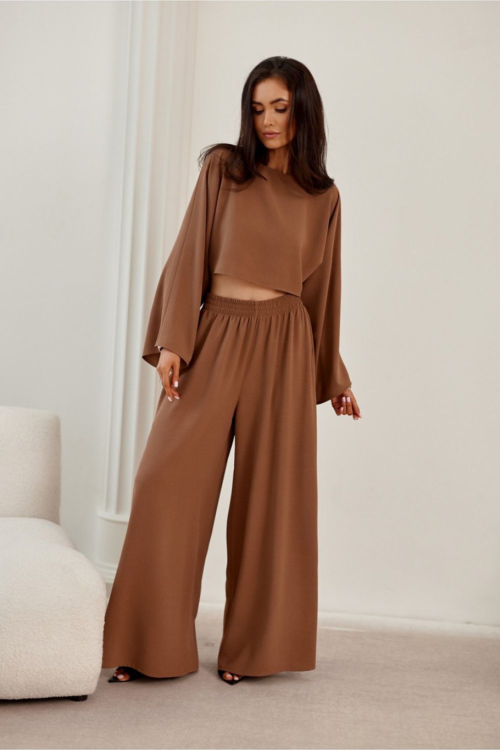 Woman wearing a brown outfit in a minimalistic room.
