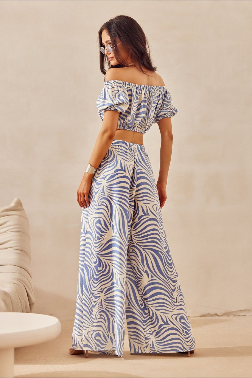 Woman wearing a patterned outfit standing against a beige wall.