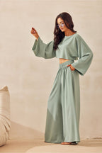 Woman wearing a light green outfit with wide sleeves and high-waisted pants against a beige background.