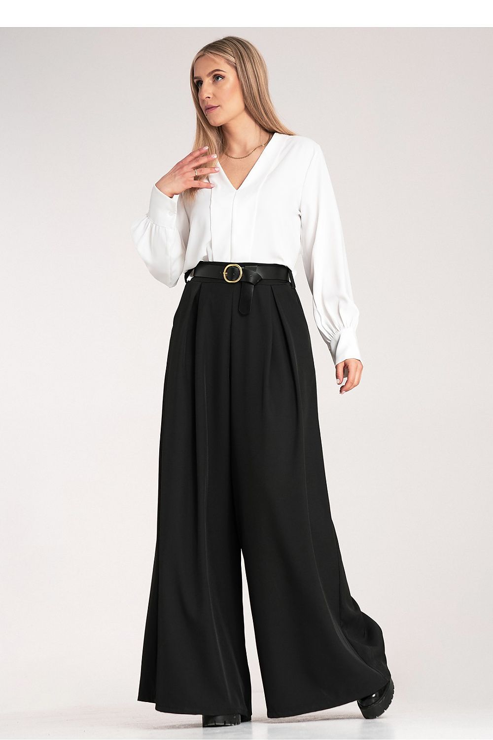 Woman wearing a white blouse and black wide-leg pants on a white background