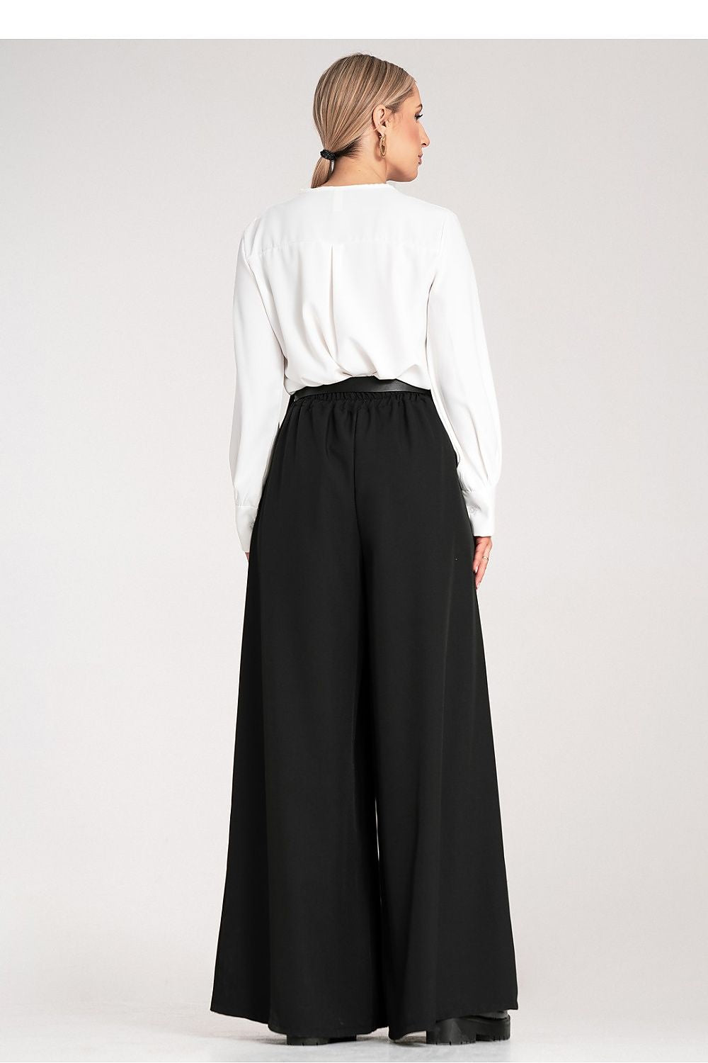 Person wearing a white shirt and black wide-leg pants on a plain background