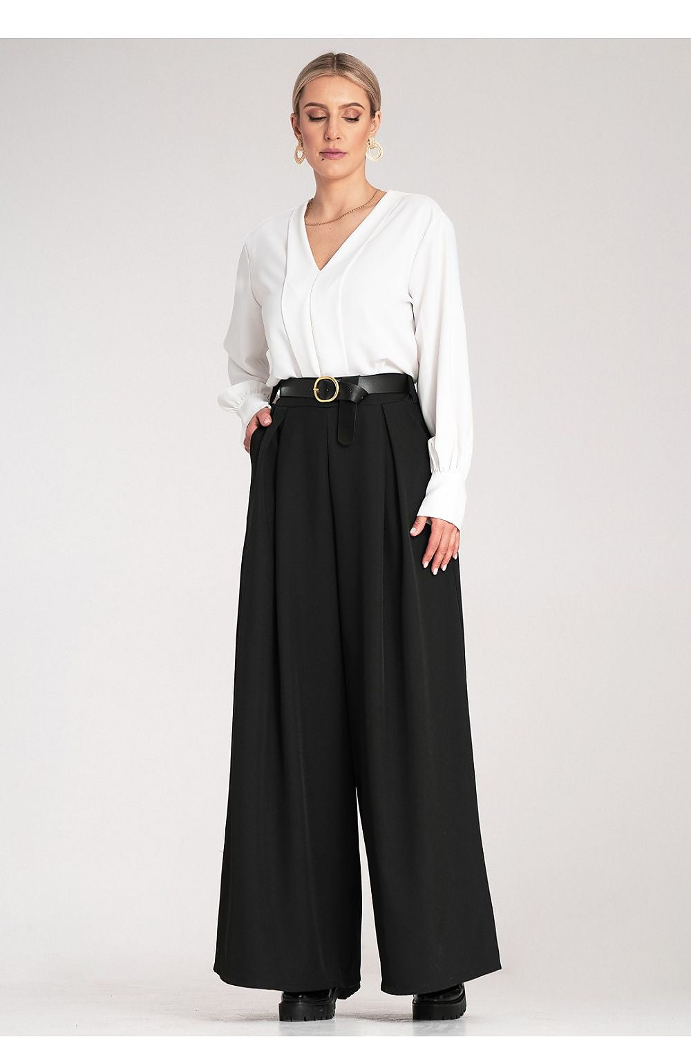 Woman wearing a white blouse and black wide-leg pants on a white background