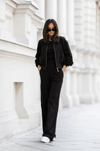 Person wearing a black outfit with sunglasses in front of a white building.
