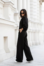 Person wearing a black outfit standing against a white architectural background