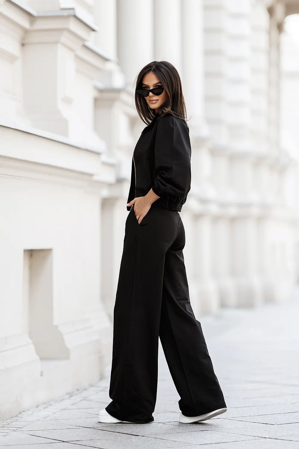 Person wearing a black outfit standing against a white architectural background