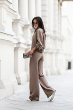 Woman in a beige outfit walking on a street with classical architecture.