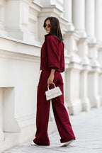 Woman in burgundy outfit holding a white handbag against a white architectural background