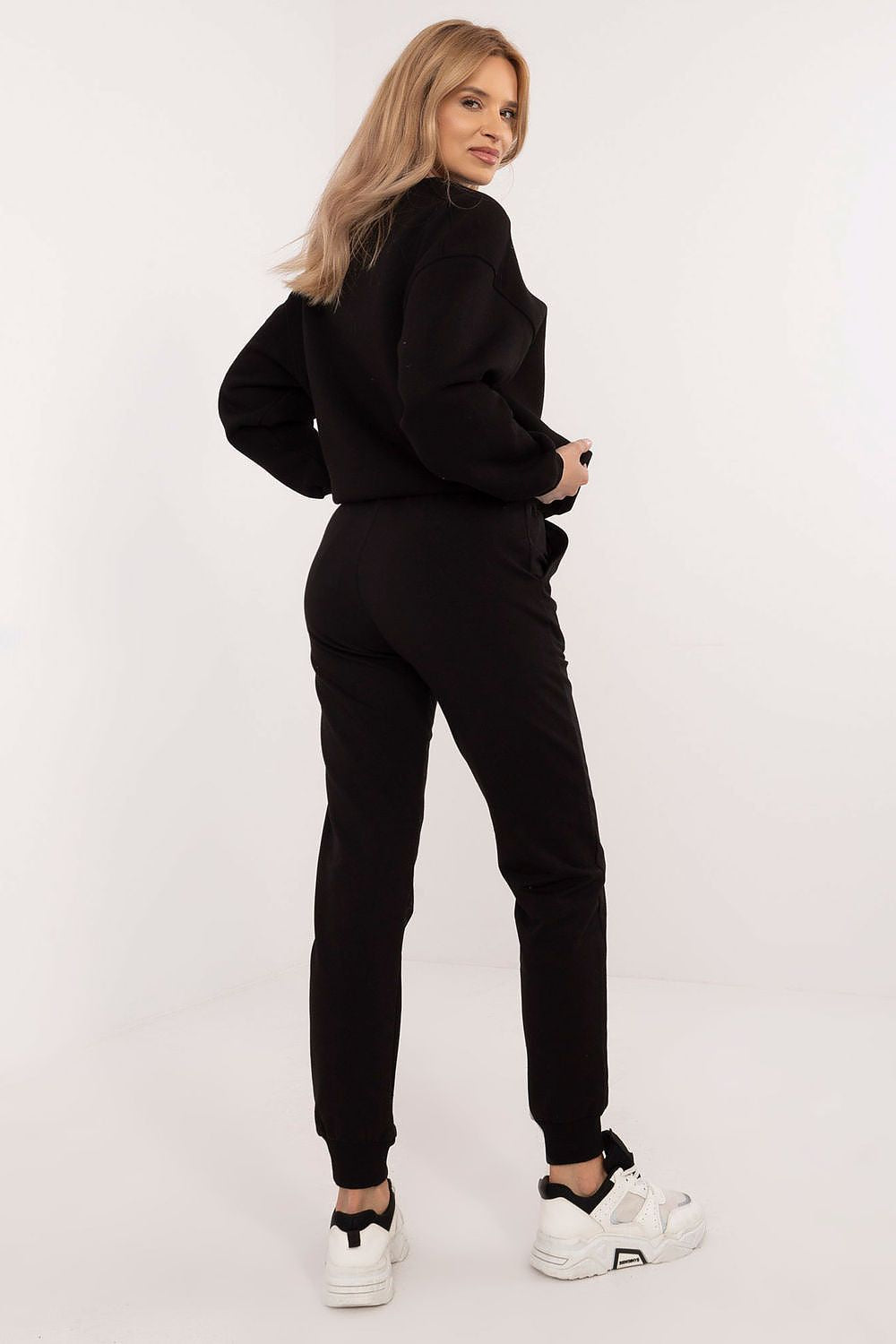 Person wearing a black tracksuit with white sneakers on a white background