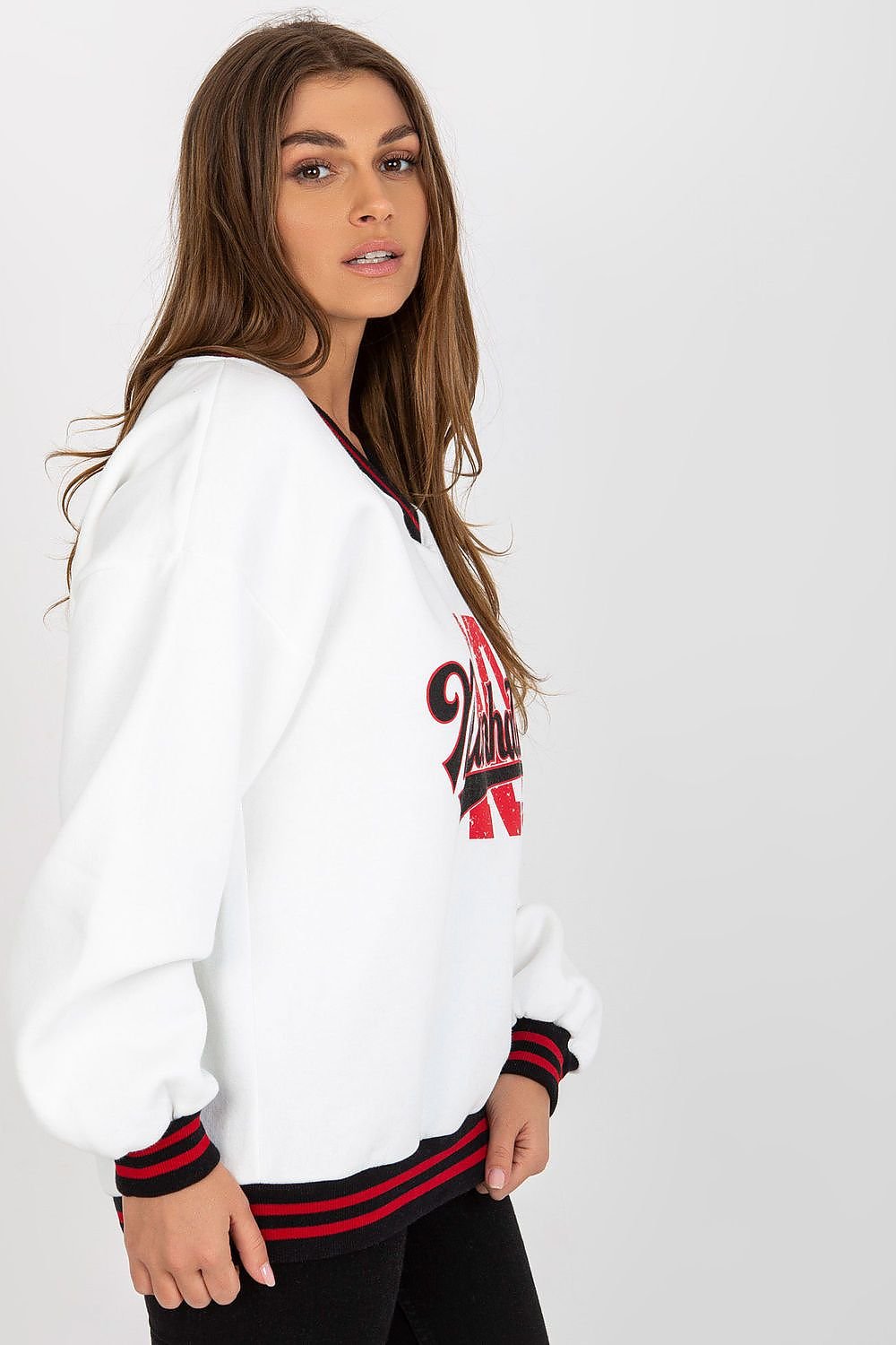 Woman wearing a white sweatshirt with red and black accents on a plain background
