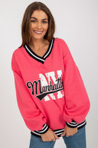 Woman wearing a pink sweatshirt with 'Manhattan' print on a plain background