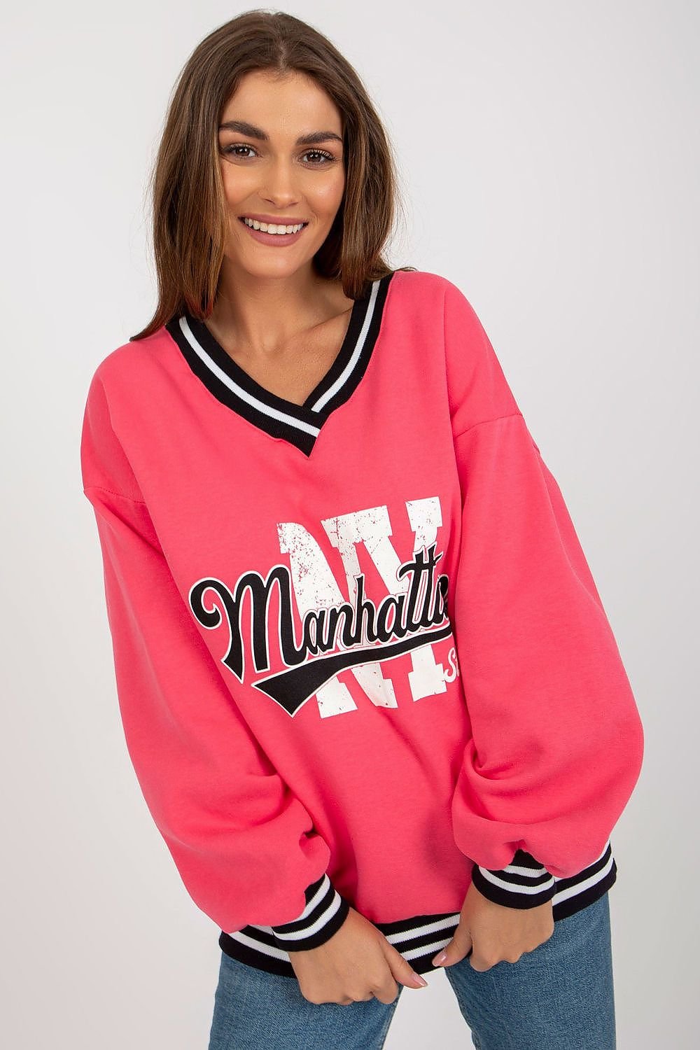 Woman wearing a pink sweatshirt with 'Manhattan' print on a plain background