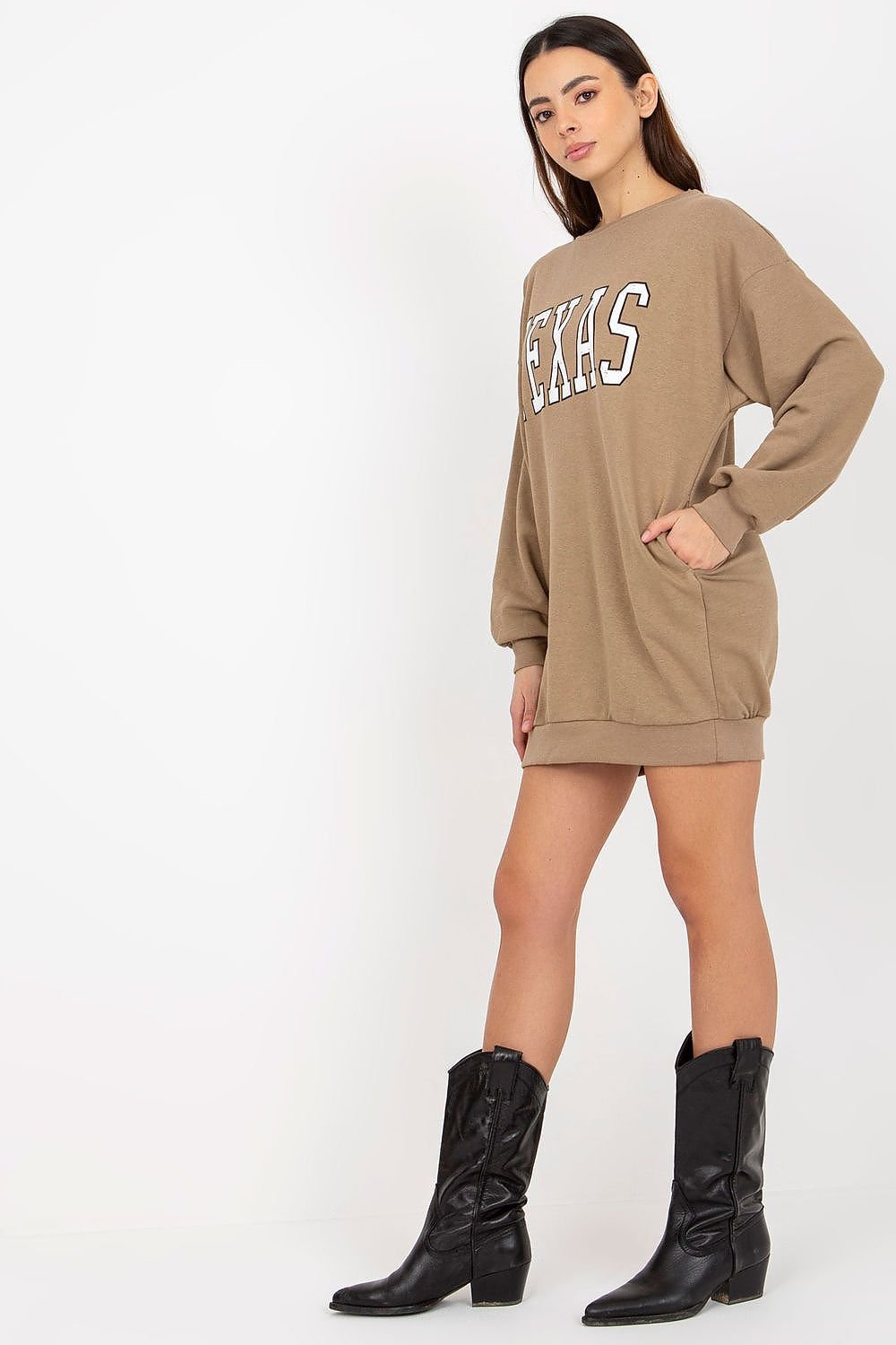 Woman wearing a beige sweatshirt dress with 'TEXAS' text and black cowboy boots on a white background