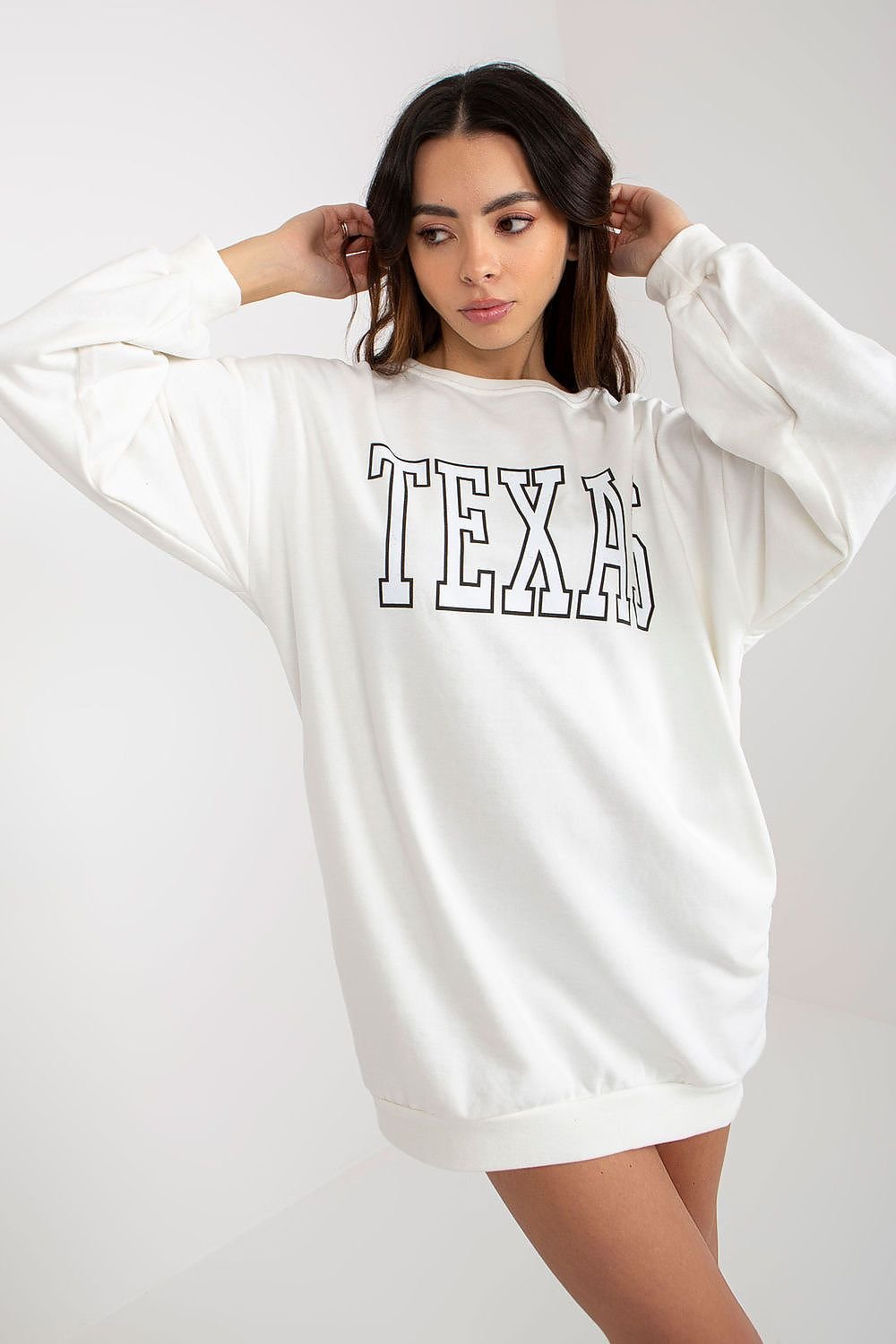 Woman wearing a white sweatshirt with 'TEXAS' printed on it against a plain background